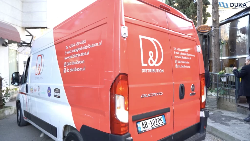 A red and white 'D&D Distribution' delivery van parked on the street, with company contact information and logos of associated brands displayed on the vehicle.