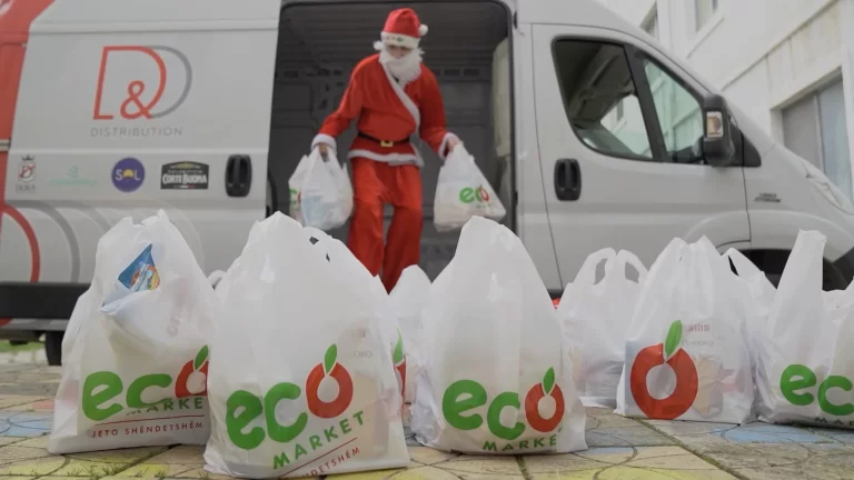 Man in a Santa Claus red costume carrying white 'eco market' branded shopping bags with a 'D&D Distribution' van parked in the background, symbolising festive season deliveries.