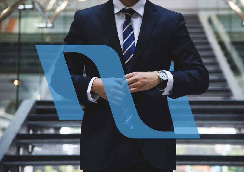 A well-dressed businessman in a sharp blue suit and striped tie, making a subtle adjustment to his cufflink while standing in a bustling corporate atrium, overlaid with a bold blue 'DUKA Group' logo.