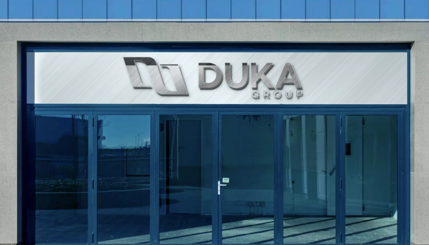 The contemporary facade mock-up of the DUKA Group headquarters, featuring a sleek glass entrance and the company's modern logo prominently displayed above the door on a clear day.